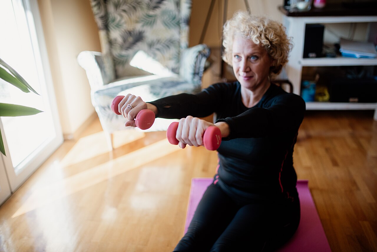 Renforcement musculaire maison : femme de 50 ans faisant des exercices avec haltères sur un tapis dans son salon