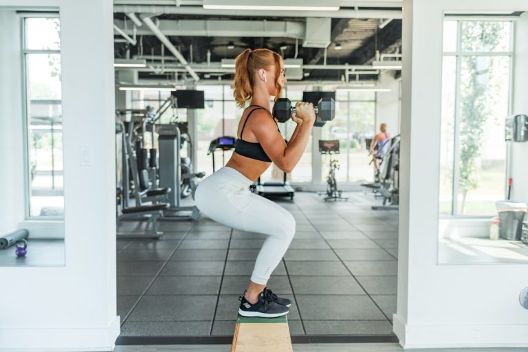 Squats bienfaits : femme en position de squat avec haltère en salle de sport