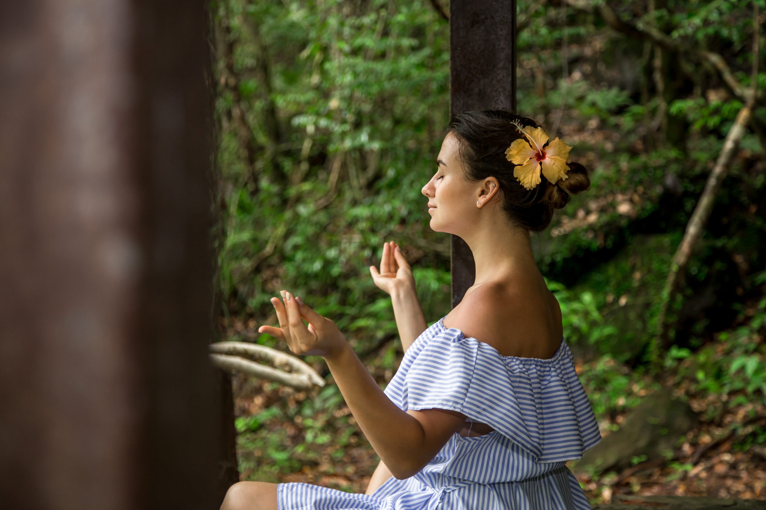 Femme méditant dans la nature, assise avec une fleur dans les cheveux, symbole de sérénité et bien-être.