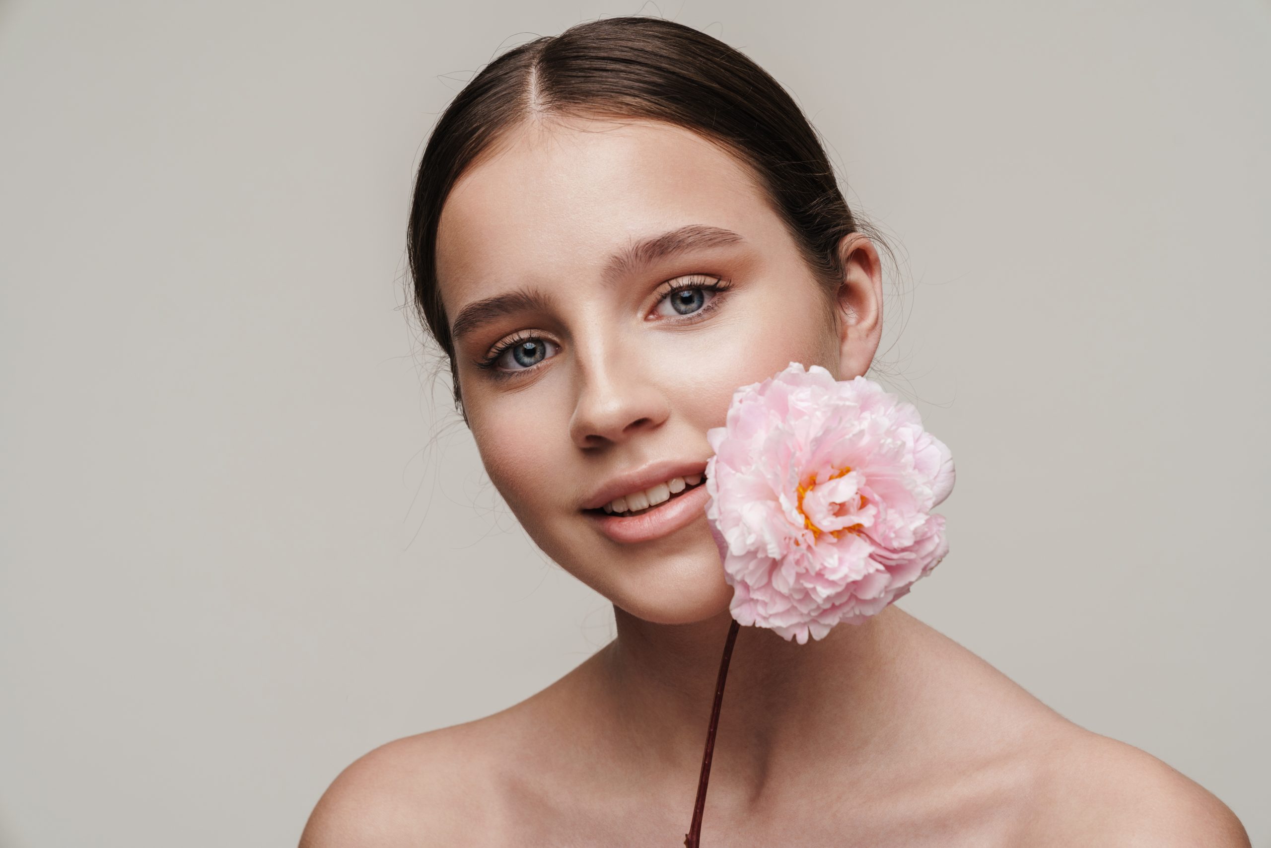 Femme souriante avec une fleur rose, symbole de beauté naturelle et de bien-être holistique.