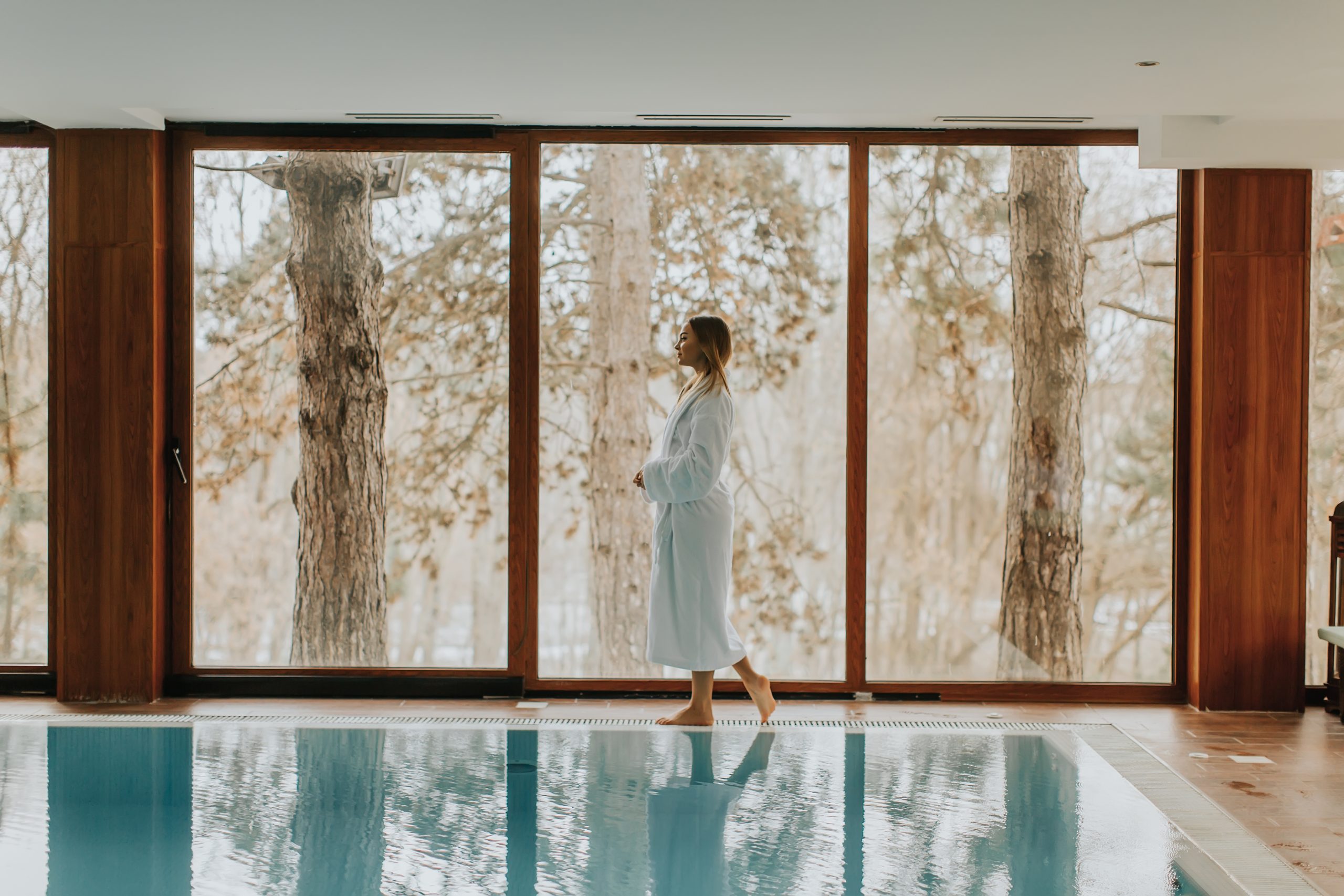 Femme en peignoir au spa près d’une piscine intérieure, symbole de détente et ressourcement.