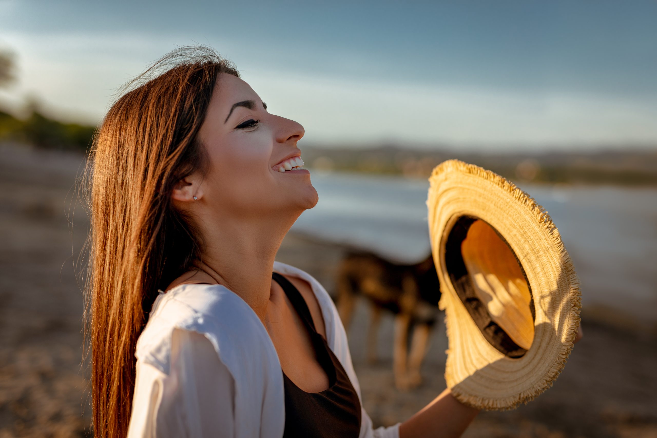Femme souriante au bord de l’eau, incarnant bien-être, détente, joie et connexion avec la nature.