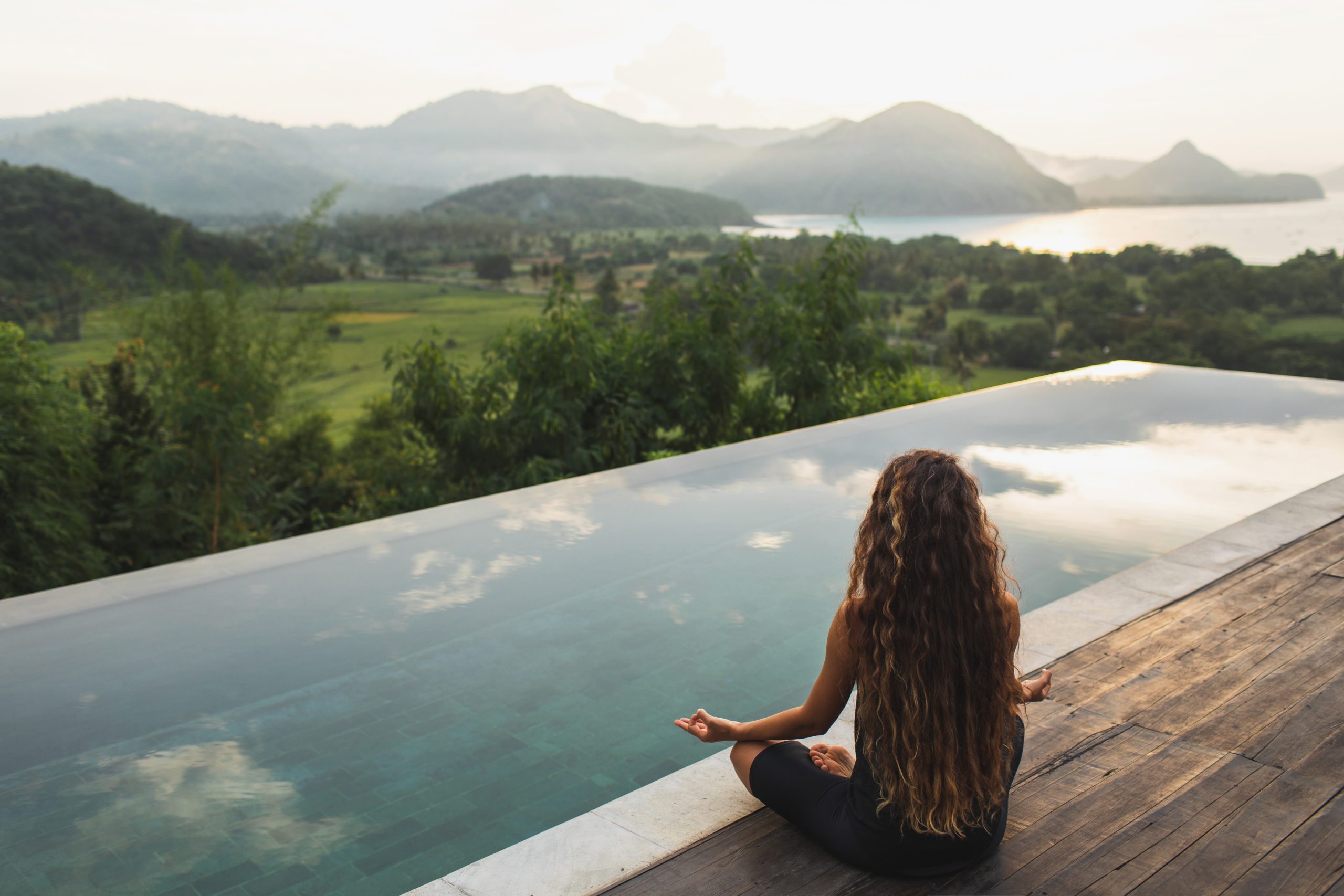 Femme méditant au bord d’une piscine à débordement, symbole de bien-être et sérénité en solo.