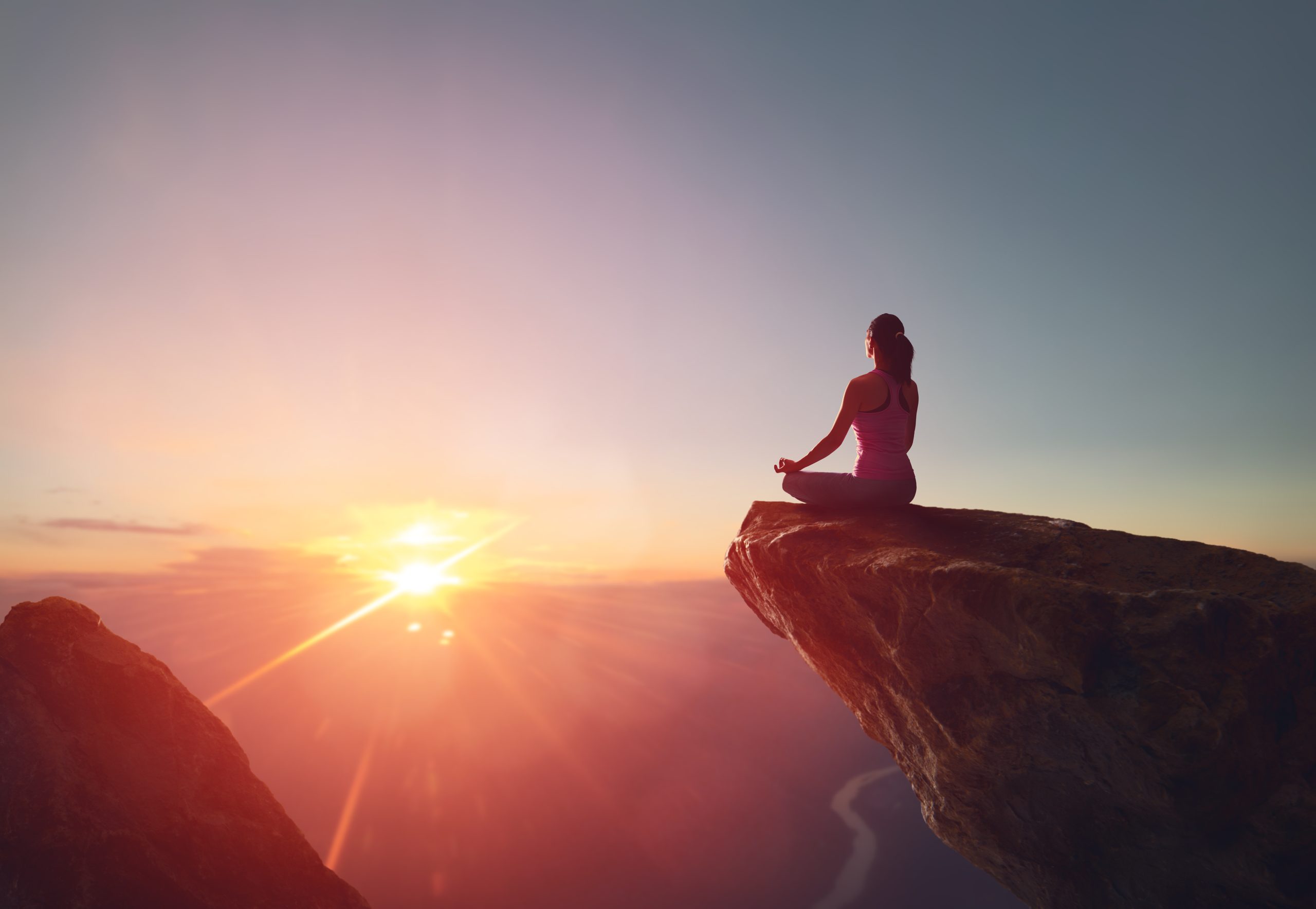 Femme méditant sur un rocher au lever du soleil, symbole de bien-être et reconnexion à la nature.
