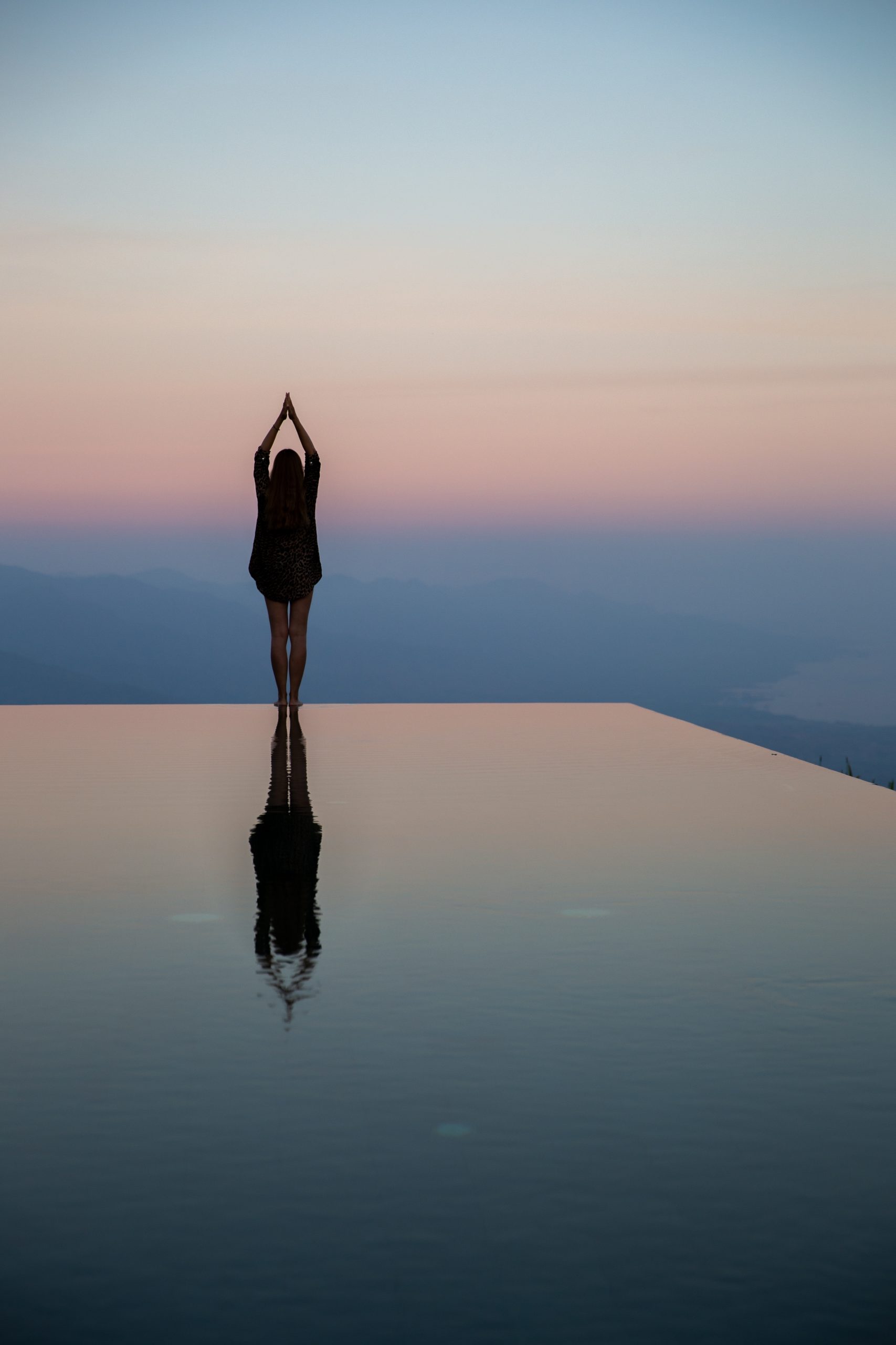 Femme au bord d’une piscine au coucher du soleil, reflet d’harmonie et bien-être apaisant.