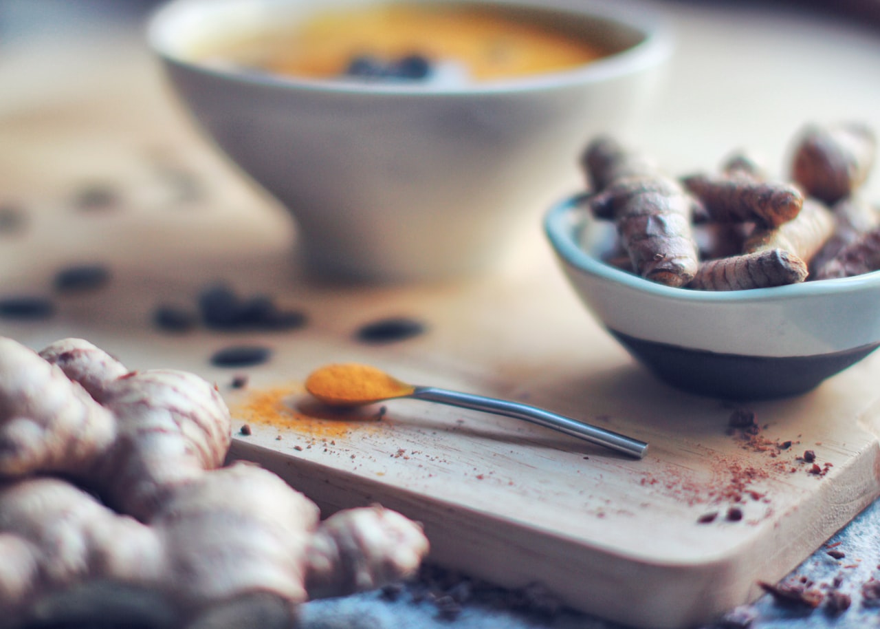Bienfaits du curcuma : lait d'or, racines fraîches et poudre de curcuma sur une planche