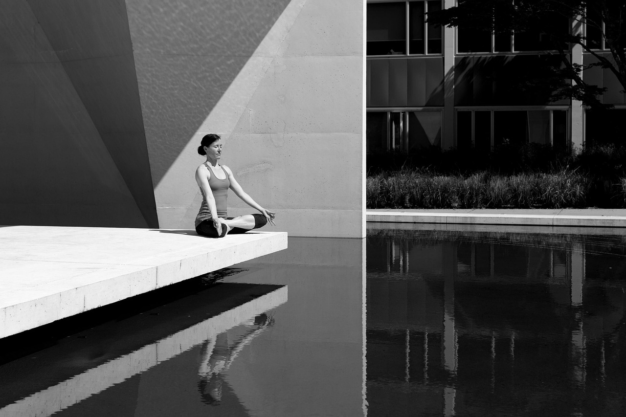 Femme méditant seule en posture du lotus au bord d'un bassin, pratique individuelle du yoga