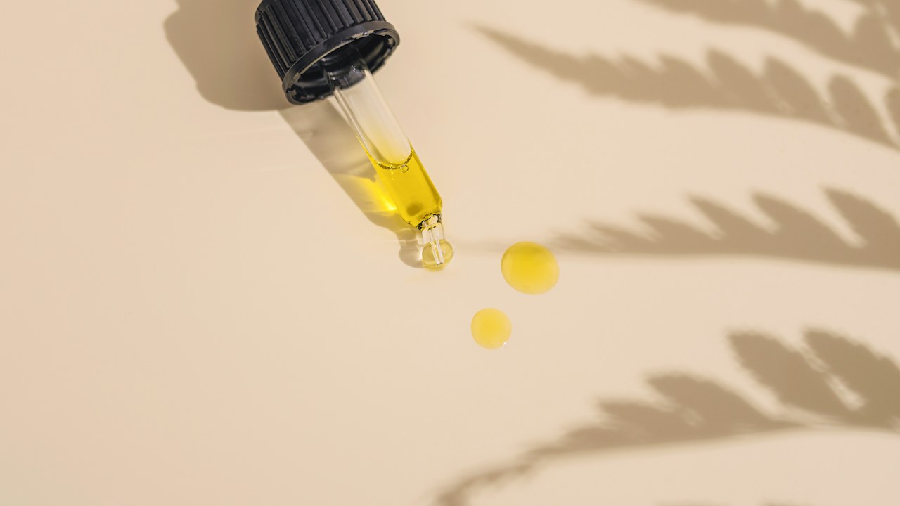 Huile de CBD qui s'écoule d'une pipette, avec l'ombre d'une feuille de chanvre